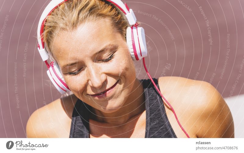 Young woman listening to music with earphones for fitness motivation. Portrait of a young woman in sportswear relaxing sitting getting inspired. gym lifestyle