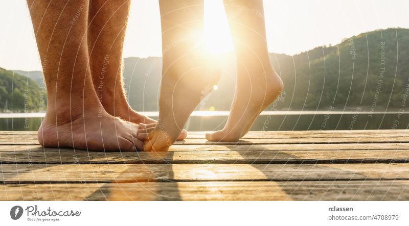 Legs on jetty. A young loving couple hugging and kissing on the pier on a lake at sunset. Two lovers, man and woman barefoot near the water on a jetty. Happy love moments together.