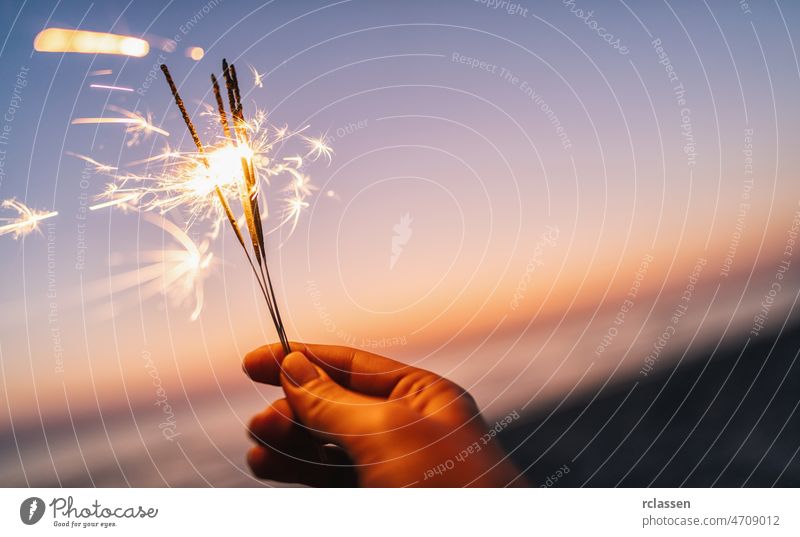 hand holding sparkler at sunset light beach firework night girl party people summer woman abstract background burning celebration flame glow young beautiful