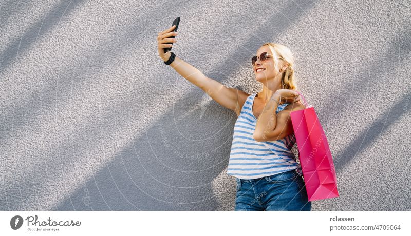 Young attractive woman taking selfie with smartphone with shopping bag after shopping. holding mobile phone and doing selfie. fashion summer 20s brunette buy