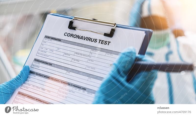 Doctor fills out a coronavirus test data sheet with pen for a patient in protective clothing in a clinic leaning at Covid-19 coronavirus epidemic doctor