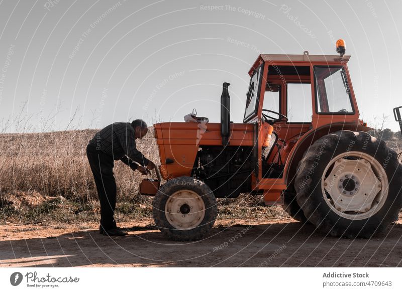 Old tractor driver taking instrument from toolkit for repair man senior work field male farmer box agriculture maintenance vehicle labor transport farmland job