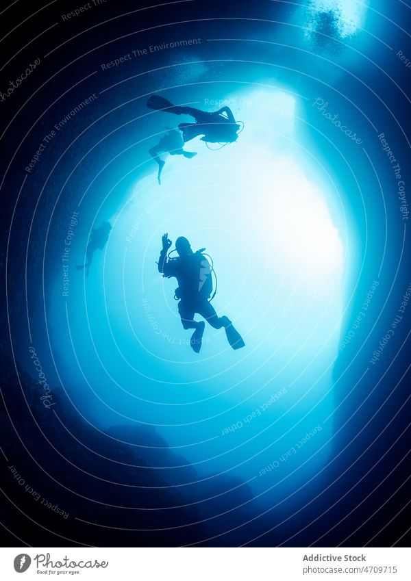 Divers swimming between rocky formations diver sea underwater cave dark explore discover deep undersea active seawater aqua activity ocean light extreme clear