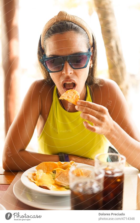 A young woman eating a portion of nachos with meat adult alcohol appetizer avocado beach beautiful caucasian chili chips cocktail corn delicious drink female