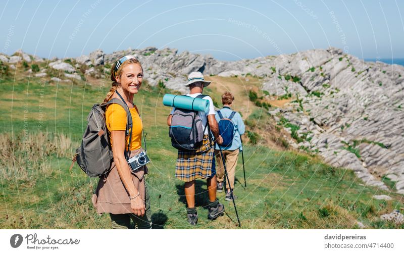 Happy young woman looking camera hiking with her grandparents happy smiling trekking family together grandfather grandmother granddaughter adult backpack group