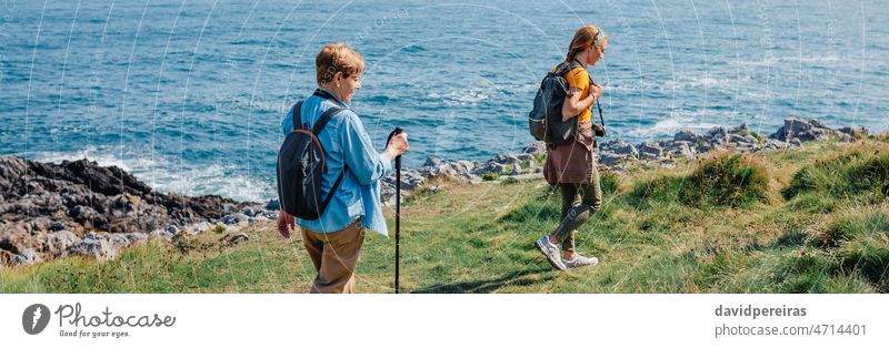 Grandmother and adult granddaughter trekking along the coast grandmother women shore sea family banner web header panorama panoramic copy space landscape senior