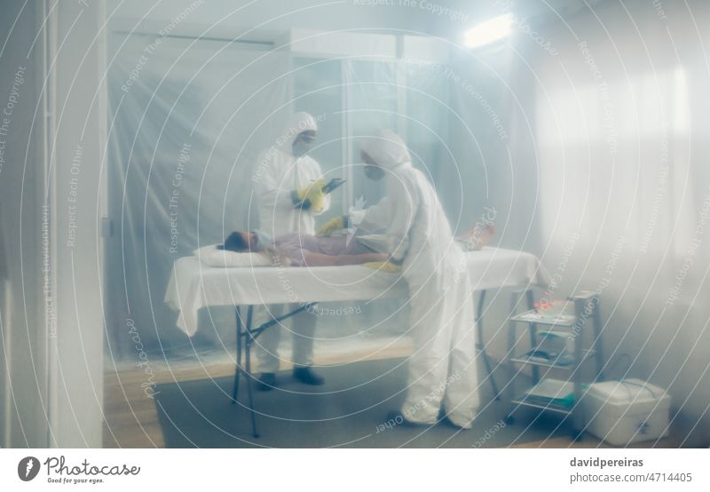 Doctors in bacteriological protection doing medical check to patient lying on a gurney field hospital isolation doctor protection suit coronavirus