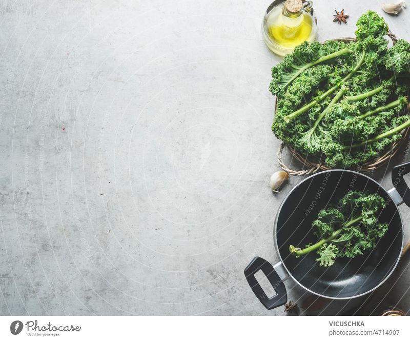 Food background with green kale leaves, black cooking pan, olive oil food background anise garlic grey concrete kitchen table healthy home seasonal winter