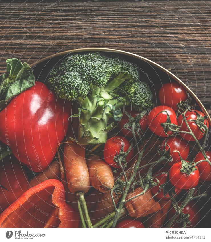 Close up of various colorful vegetables in bowl at rustic wooden kitchen table close up red bell pepper broccoli carrots tomatoes healthy cooking home organic