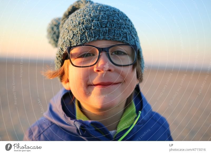 child wearing glasses looking curious at the camera and smiling Emotions Mysterious Identity Uniqueness Smiling face smilingly laughing child fortunate joyfully