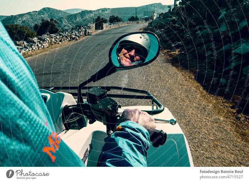 Quad bike rider with helmet in rear view mirror with hand on throttle on a Greek road Driver Face Rear view mirror Gas hand Man 50 - 60 years old Smiling