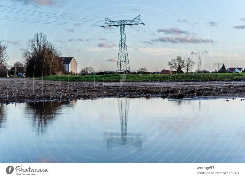 High voltage power line at the edge of the village reflected in a puddle of rain Power lines high-voltage pylons Overhead line Reflection in the water Puddle