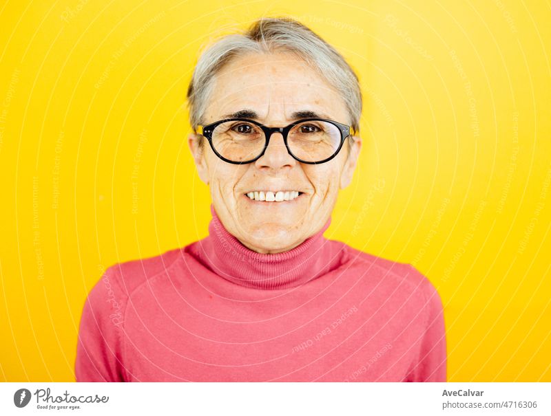 Old woman close up smiling to camera happy posing isolated over yellow color wall background. Daily expressions with copy space in studio. old caucasian