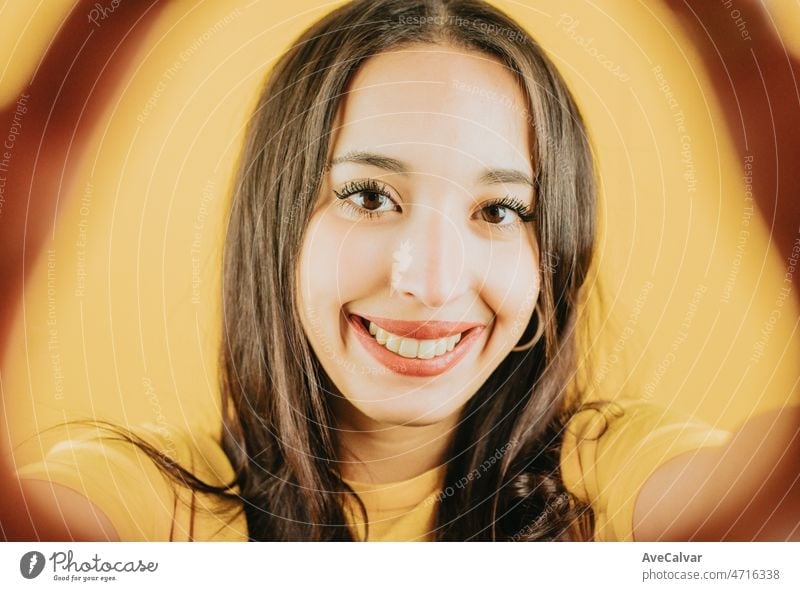 Young african woman holding the camera taking a selfie smiling to camera happy and cool attitude concept posing isolated over yellow color wall background. Daily expressions with copy space in studio.