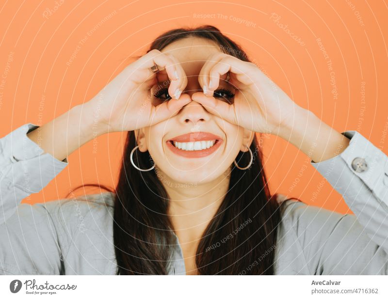 Young african woman using his hands as binoculars smiling to camera looking for something posing isolated over orange color wall background. Daily expressions with copy space in studio.