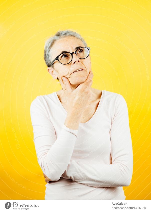 Old woman thinking about something serious and worried about it posing isolated over yellow color wall background. Daily expressions with copy space in studio.