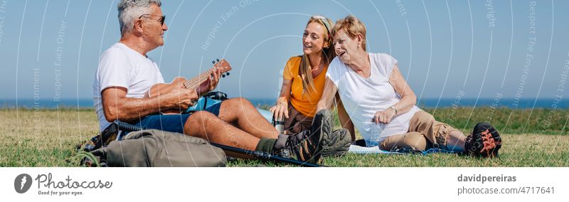 Adult family playing ukulele and singing sitting on a blanket during an excursion adult musical instrument banner web header panorama panoramic outdoors happy