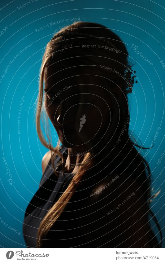Portrait of woman with long blond hair against blue background. Face shrouded in darkness as anonymous silhouette Woman portrait Dark Shadow contours Lowkey