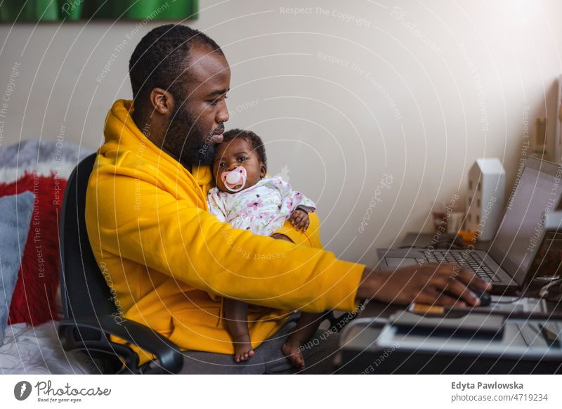 Man holding his newborn baby girl and working with laptop at home father dad kids child family fatherhood real people indoors house flat apartment enjoy adult
