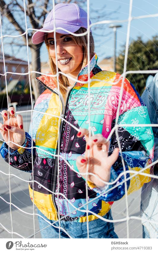 Female clutching the fence wearing a multicolored jacket female basketball court cap woman person outdoor beautiful adult attractive girl lady young beauty