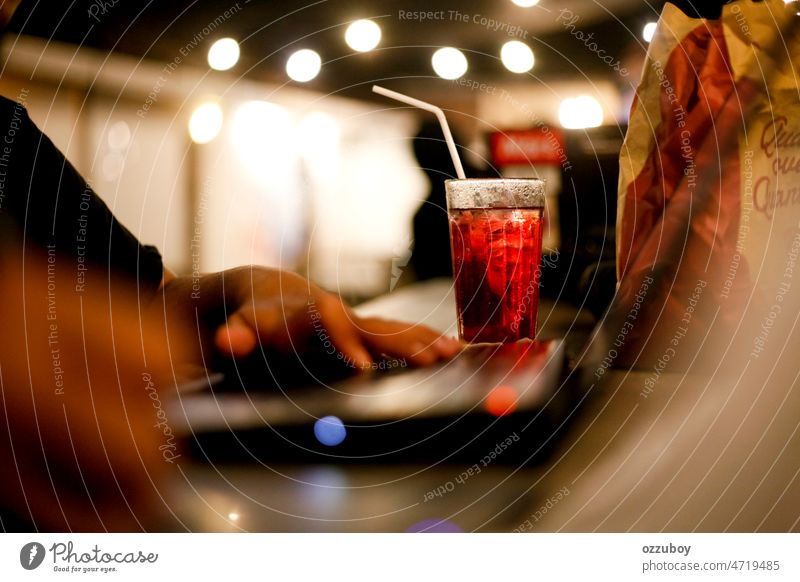 Selective focus of strawberry tea ice drink with blurred hand freelancer working on laptop at late night in cafe person computer business modern technology