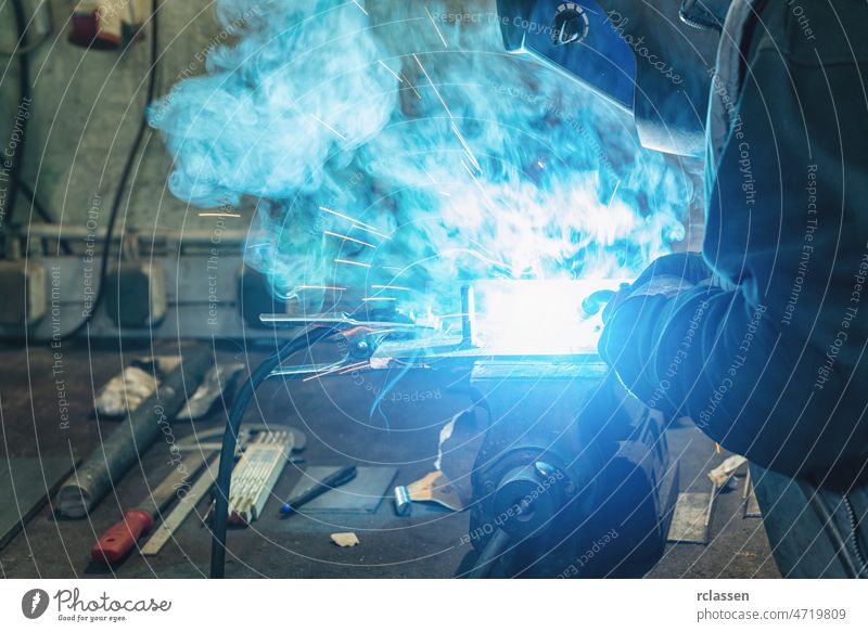 A man welder with construction gloves and a welding mask hard work and welds with a welding machine metal in workshop, close up assembly equipment labour line