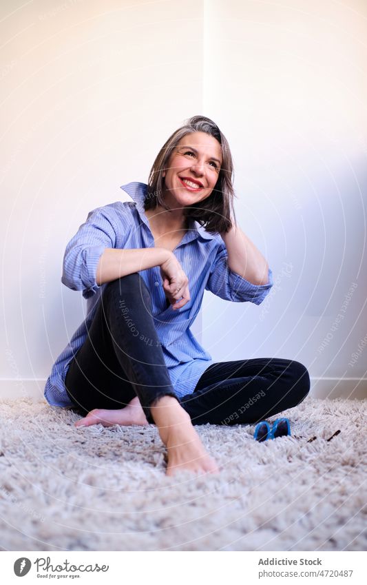 Cheerful woman sitting on carpet style feminine appearance smile design room apparel trendy garment wall home apartment barefoot lady glad light positive female