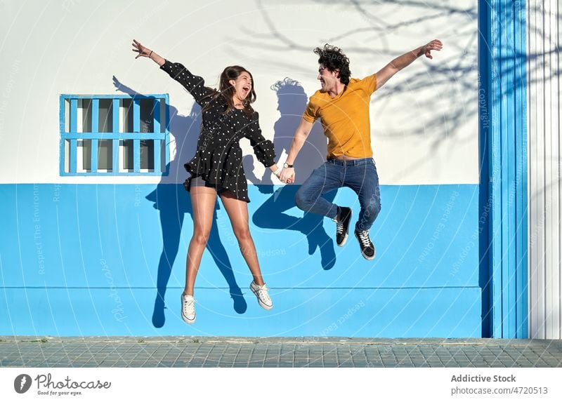 Cheerful couple jumping near wall having fun activity relationship love street leisure bonding fondness affection together young happy boyfriend girlfriend