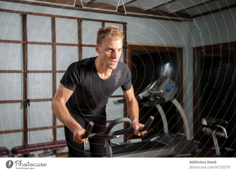 Confident man exercising on cycling machine in gym sportsman cycle exercise training workout determine confident fit male fitness athlete physical activity