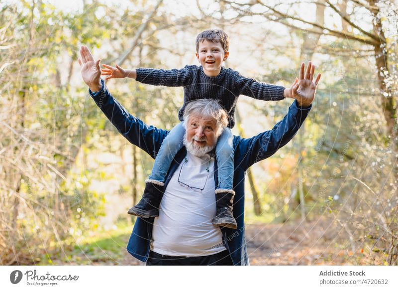 Cheerful senior man with grandson on shoulders in forest smile child park kid hold autumn boy positive together male happy cheerful grandfather elderly aged