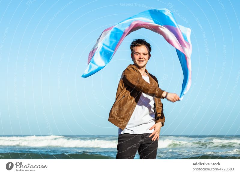 Content man with colorful transgender flag near sea lgbtq identity freedom equal coast nature seashore male beach water wave seaside ocean optimist eyes closed