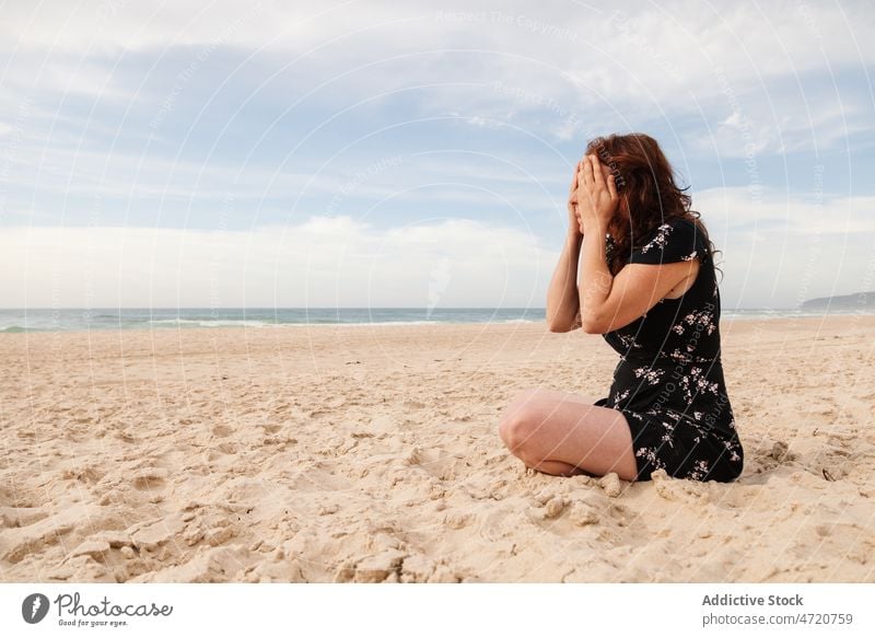 Woman sitting on beach covering her eyes with her hands woman shore sea seashore recreation pastime leisure rest tourist resort sand seaside seacoast water