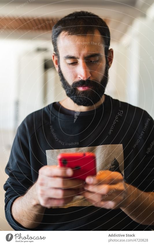 Bearded man in sweatshirt browsing smartphone using text message online surfing check read internet gadget male texting modern casual cellphone device mobile