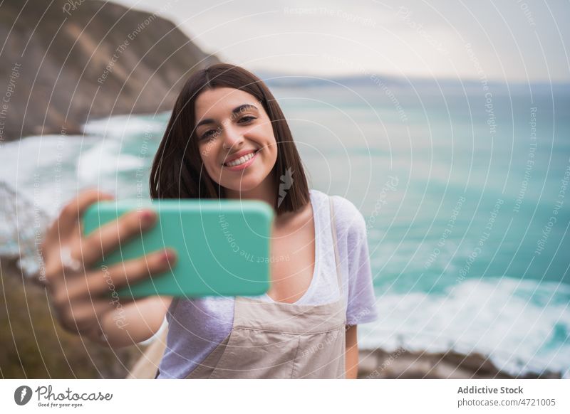 Cheerful woman taking selfie on seashore coast pastime trip smartphone photography capture memory self portrait leisure adventure travel seaside feminine