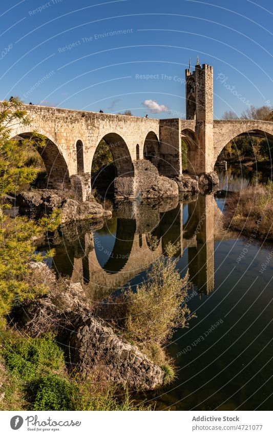 Old bridge over river against town in mountainous area landscape sightseeing formation ancient construction travel spain girona picturesque cloudless idyllic