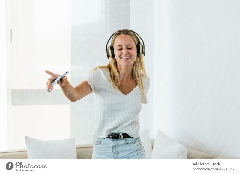Cheerful woman listening to music in headphones living room meloman playlist song hobby melody enjoy smartphone home wireless cheerful smile positive device