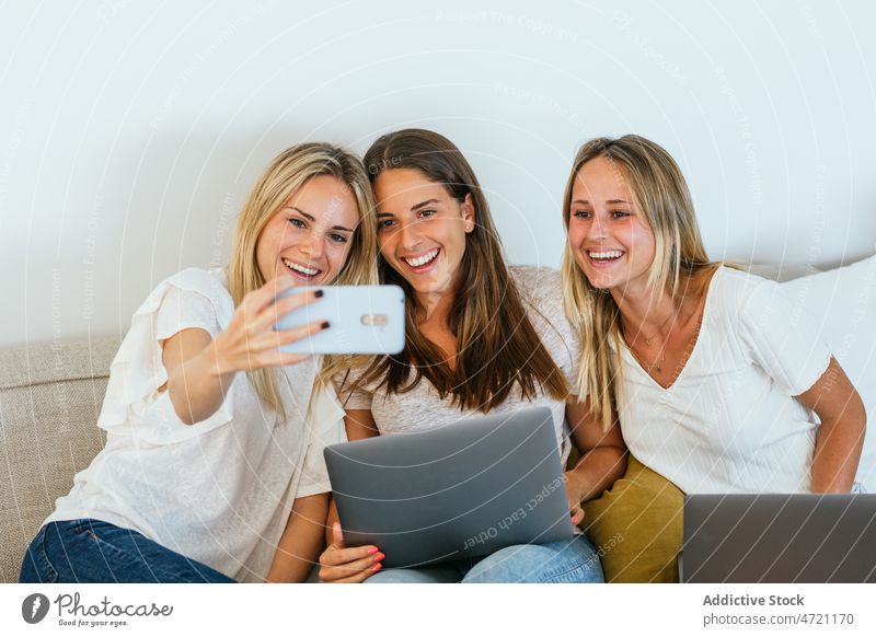 Woman taking a selfie with her sisters women friendship smartphone pastime online living room couch internet home bonding spend time glad style apartment