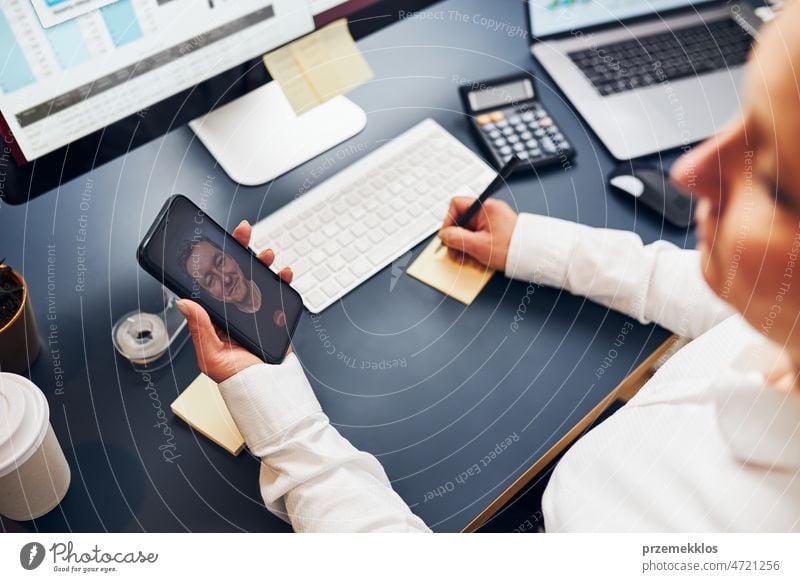 Woman entrepreneur having business video chat on smartphone. Businesswoman making notes while talking to her co-worker call colleague conversation calling