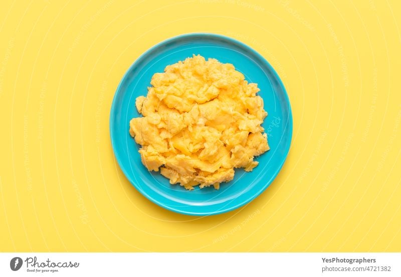 Scrambled eggs in a blue plate, top view on a yellow table. above american background breakfast bright brunch close-up color copy space creamy cuisine delicious