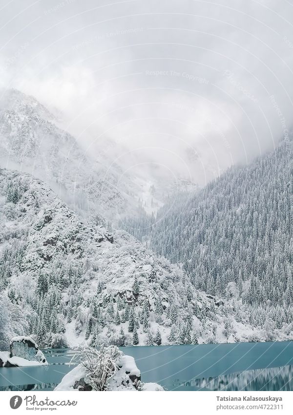 ice-covered turquoise water of a mountain lake against the backdrop of mountains in fog and clouds forest Ice Snow Issyk Kazakhstan Almaty Middle Asia north
