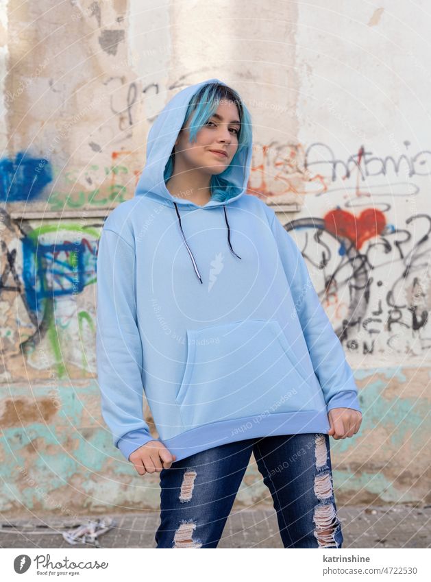 Blue haired Teenage girl in light blue oversize hoodie staying against graffiti wall Teenager mockup jeans blue haired teen girl outdoors urban modern hipster