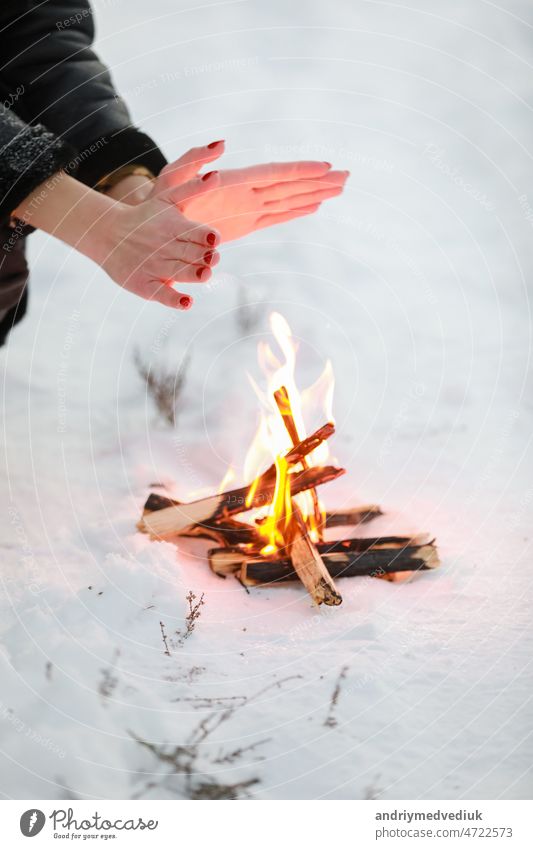 cropped photo of young woman warms her hands over bonfire in winter forest. Close-up outdoor snow cold nature travel female picnic girl happy lifestyle wood