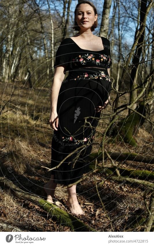 Young pregnant woman standing barefoot in forest in black maternity dress Young woman Woman pretty Beauty & Beauty Pregnant new life Life Dress Barefoot