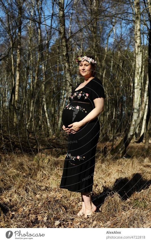 Young pregnant woman standing barefoot in forest in black maternity dress and flower wreath Young woman Woman pretty Beauty & Beauty Pregnant new life Life