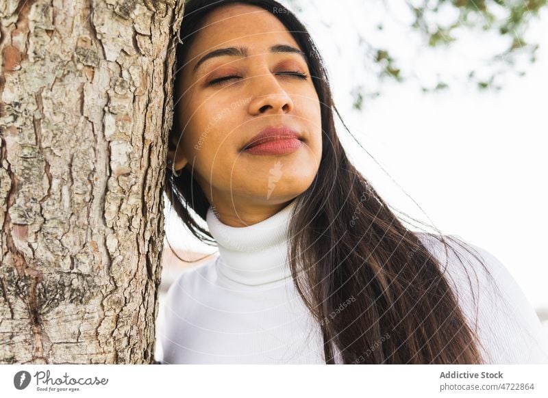 Smiling Indian woman near tree appearance street city urban branch feminine style trunk district long hair smile closed eyes attractive female charming content