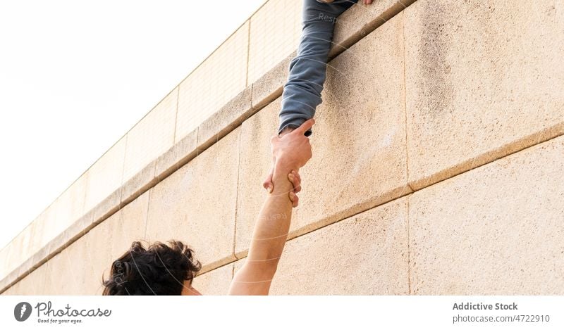 Crop person holding hand of man on building roof strong together help athlete holding hands clasp grip support parkour male guy street power unrecognizable
