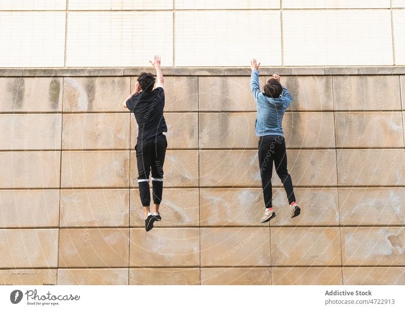 Two anonymous athlete men taking up on jumping on roof building man workout arms raised wall fit street activity male guy training exercise energy practice