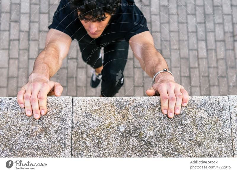 Man holding hands to wall and hanging man training street fit athlete city male guy parkour exercise fitness border sportsman urban workout strong stone