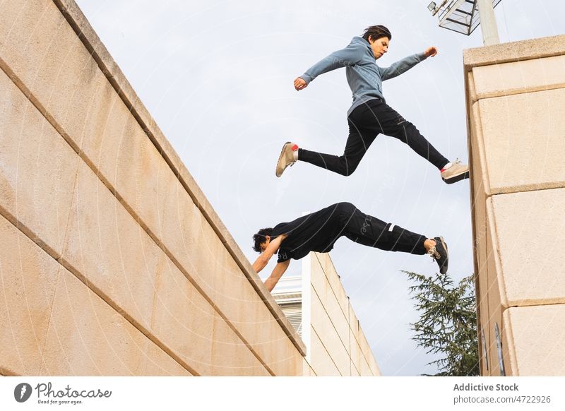 Strong guys jumping on building roof in city man parkour training extreme active street border male men leap trick unrecognizable anonymous faceless urban
