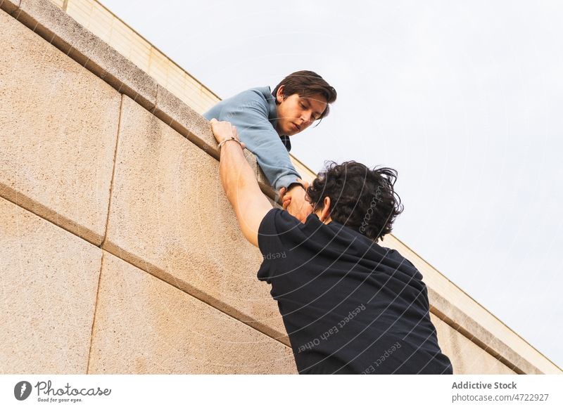 Man holding hand of man on building men roof strong together help athlete holding hands clasp grip support male parkour guy street power unrecognizable